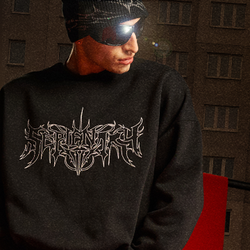 A person wearing a black sweatshirt with a graphic design that features stylized, sharp-edged text resembling a metal band logo. The background includes building windows and a red element. The focus is on the sweatshirt's design. banner