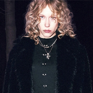 Woman wearing layered necklaces and a textured coat, presenting a bold, contemporary fashion style