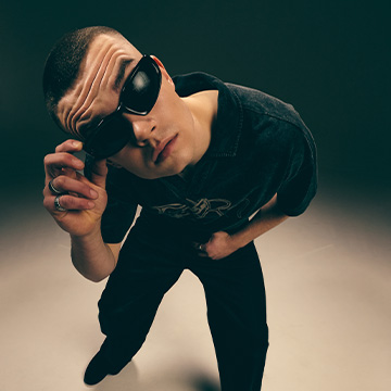 Osoba se naginje prema naprijed i usmjerava kameru prema promatraču, prenoseći razigranu, dinamičnu perspektivu i čin fotografiranja.