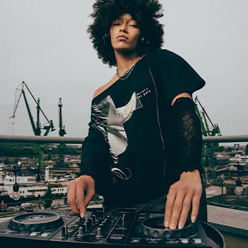 DJ performing music on a rooftop, presenting an urban streetwear style and nightlife atmosphere