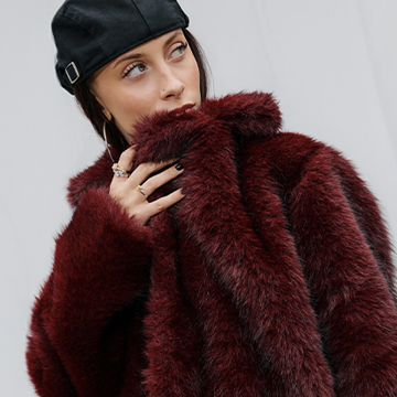 A person wearing a stylish faux fur coat and a black cap is shown, highlighting a cozy and fashionable outfit perfect for colder weather. The focus is on the textured material of the coat and the casual yet elegant vibe it portrays. banner